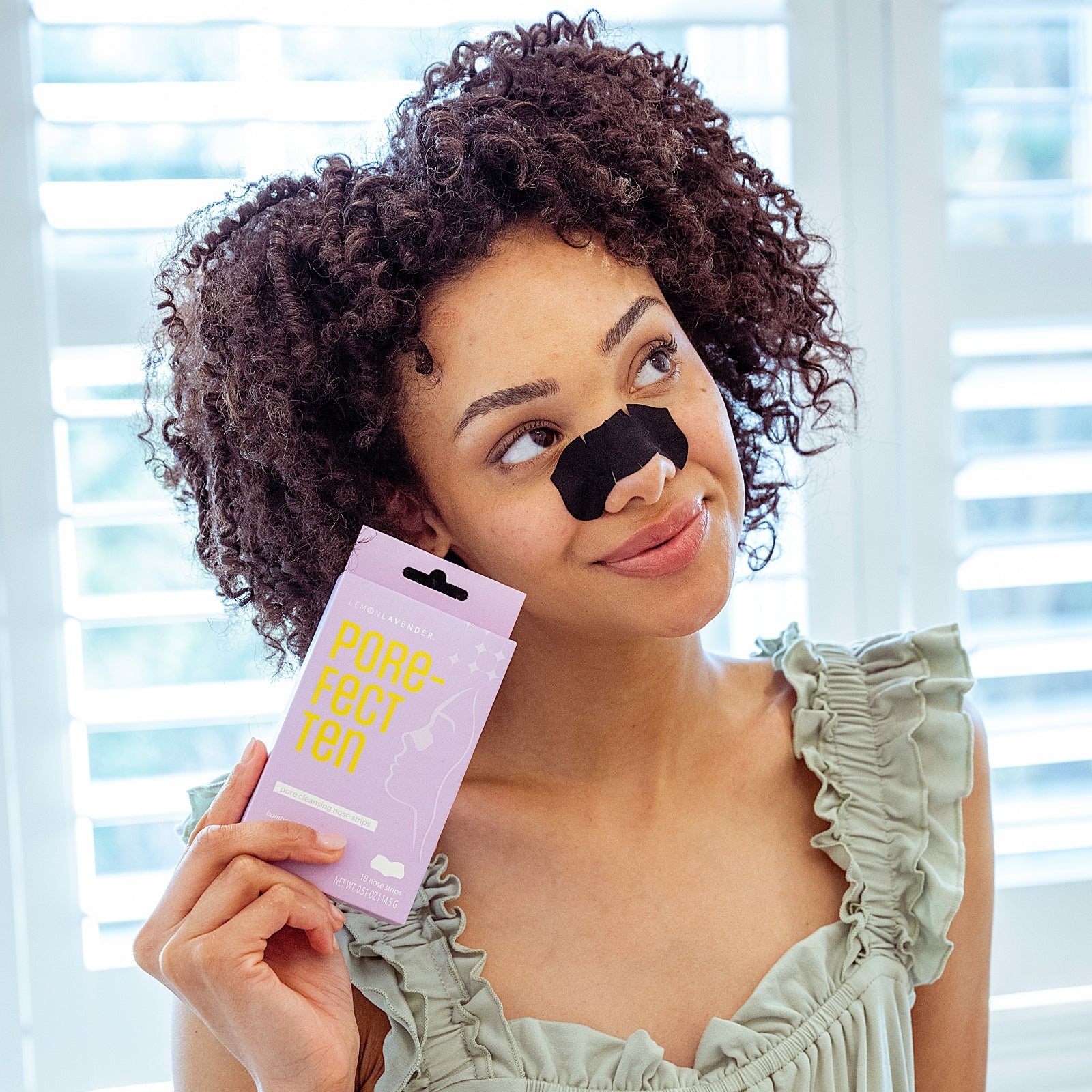 Woman applying a pore strip with 'Pore-fect Ten' packaging in front of her.