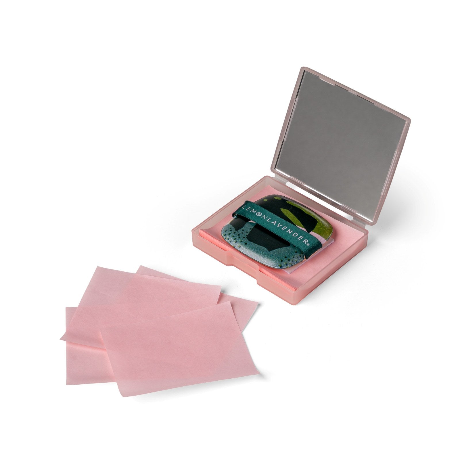 Open pink Lemon Lavender oil blotting case with a mirror, green tropical print puff applicator, and pink blotting sheets arranged beside it